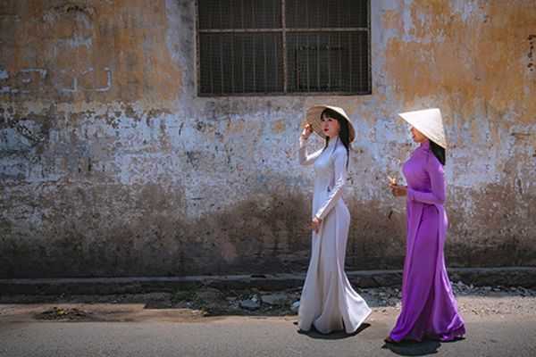 Two Asian women in long, flowing dresses walking down a concrete-lined street
