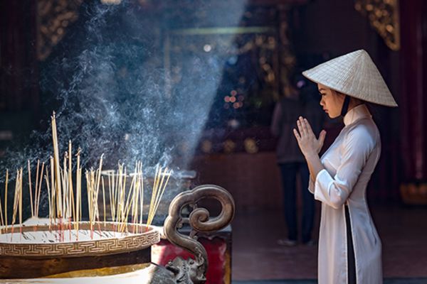 Woman wearing a straw hat praying in front of a circle of incense