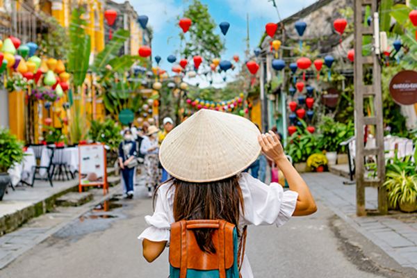 Person wearing a straw hat walking through a market street lined with blue and red hanging balloons