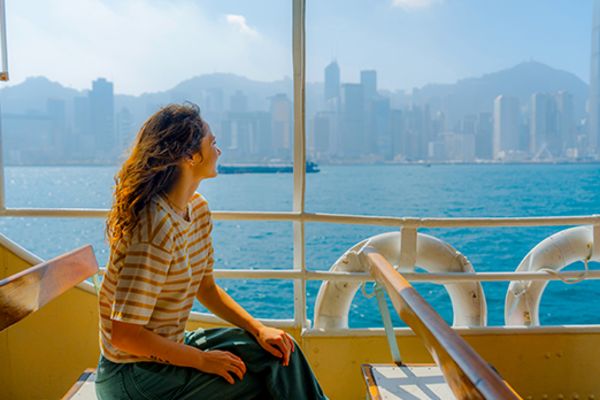 Person with long, curly hair in a stripped shirt looking at the city of Hong Kong from a boat