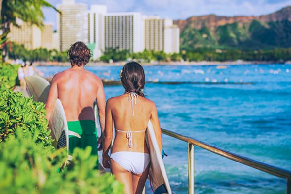 Two surfers carrying surfboards walking towards a city and the beach