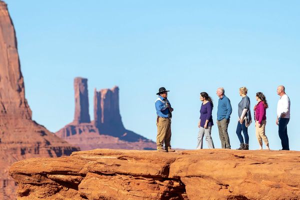 Man leading a tour group atop a large, red rock
