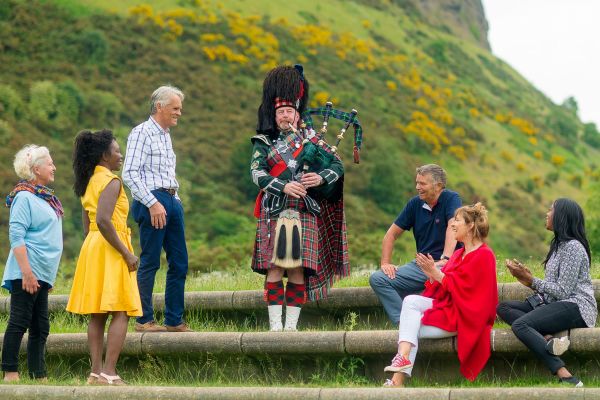 People standing around a man playing bagpipes
