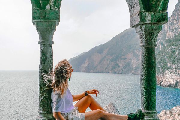 Girl sitting in a green archway looking out at the ocean