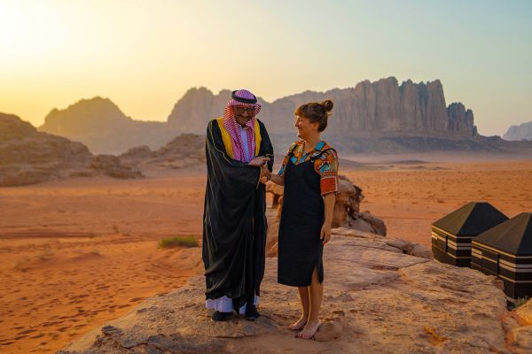 Two people standing on a rock in the desert at sunset