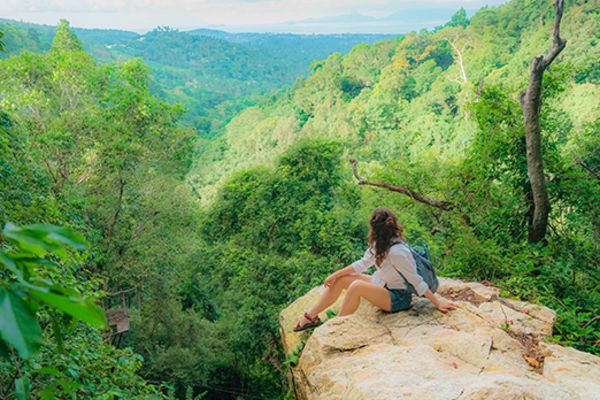 Lady sitting on edge of cliff overlooking forest in Koh Samui