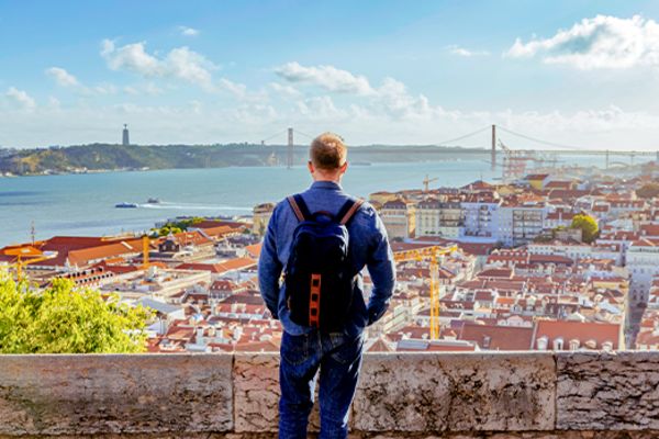 Man looking out at the city of Lisbon with a suspension bridge in the distance