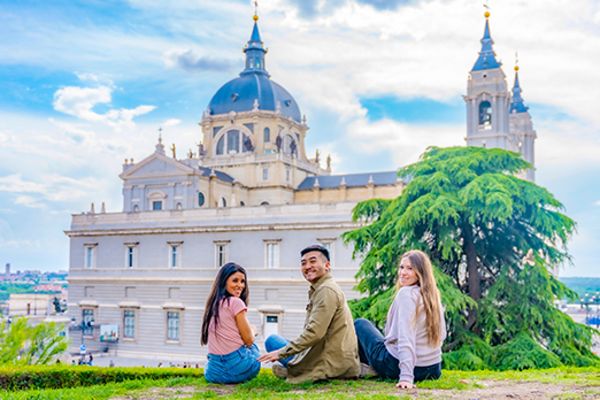 Three friends posing for a photo on a hill with Catedral de Santa María la Real de la Almudena Cathedral in the background