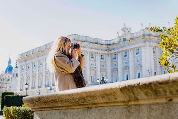 Woman taking a picture with the Royal Palace of Madrid in the background