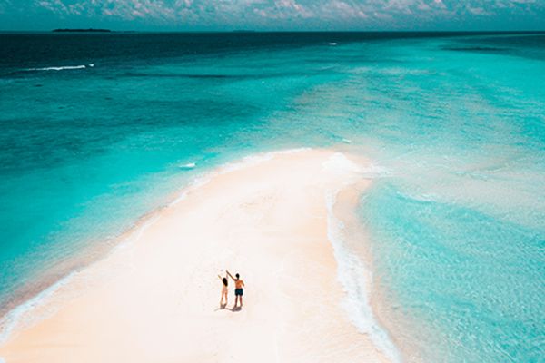 Wide shot of two people holding hands on a sandbank
