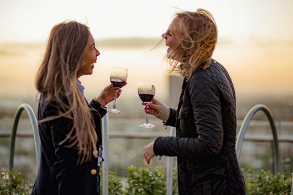 Female couple laughing, drinking wine at sunset