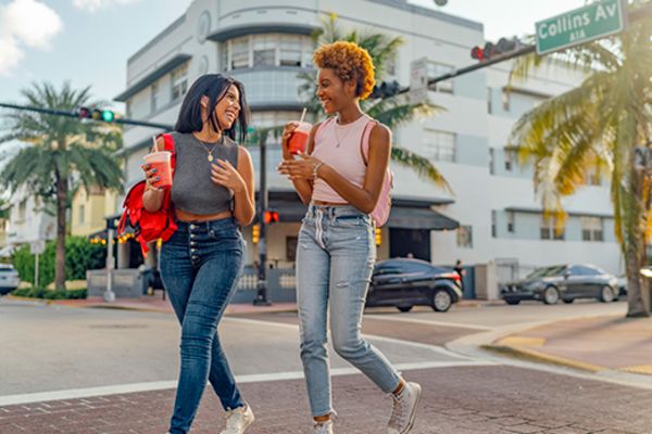 Two friends drinking smoothies while crossing a street in Maimi