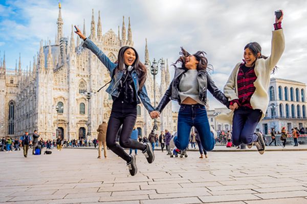 Three friends cheering and jumping into the air in front of Duomo di Milano Cathedral in Milan