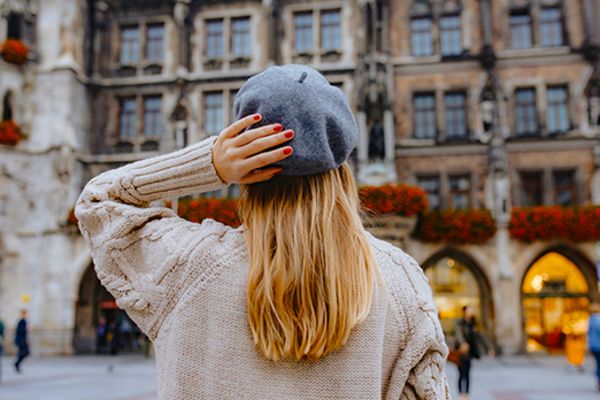 Person with red nails, long hair and a beret looking up at architecture in Munich