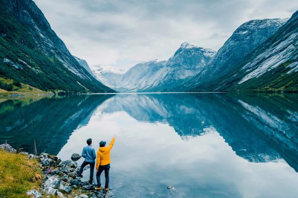 Two people on edge of lake surrouned by snow-capped mountains