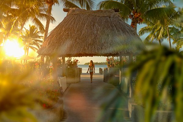 Picture of a woman in a beach bungalow at sunset taken from behind some bushes