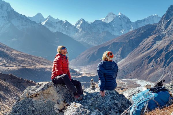 Two people in warm jackets looking at tall, snow-capped mountains