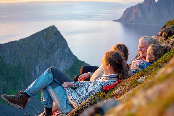 Four women relaxing on a steep cliff overlooking the sea at early sunset