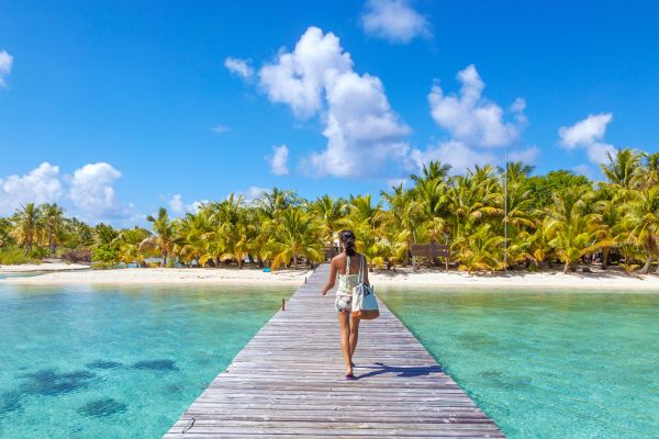 Woman walking along a pier towards a tropical island over clear blue water
