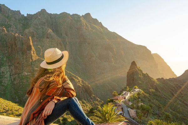 Woman sitting on a wall looking out at mountains at sunset