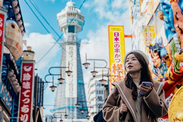 Woman in a busy shopping street in Osaka with Tsutenkaku Tower in the background