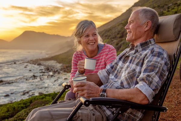 Elderly couple drinking tea in folding chairs looking out at the ocean under a sunset