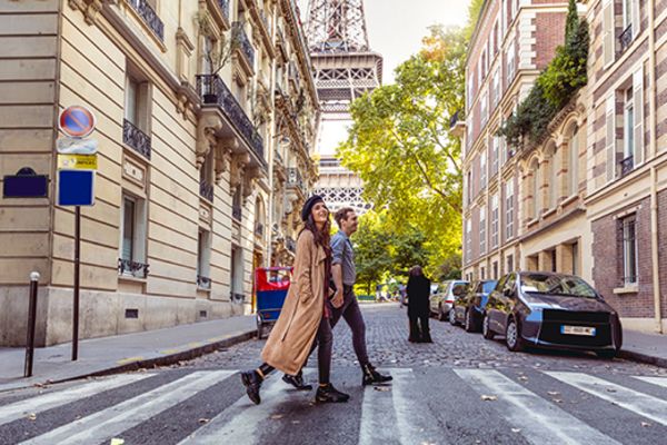 couple walking across road in paris with eiffel tower in background