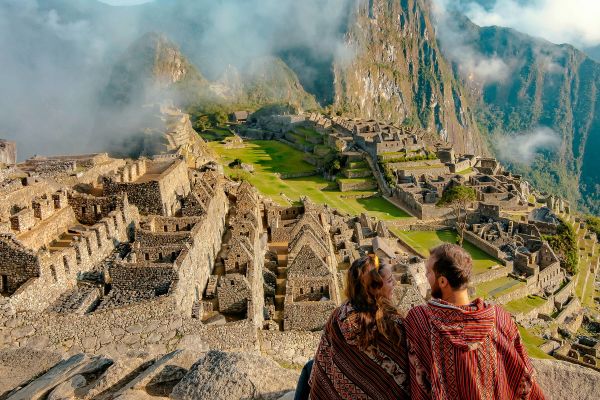 Couple dressed in ponchos watching the ruins of Machu Picchu, Peru