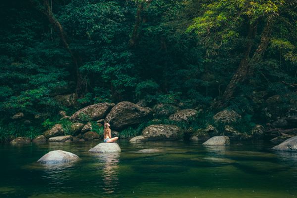 Lady sitting on a smooth rock in a lake in the middle of a rainforest