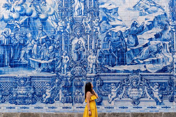 Woman in a yellow dress walking past an intricate blue and white mosaic wall