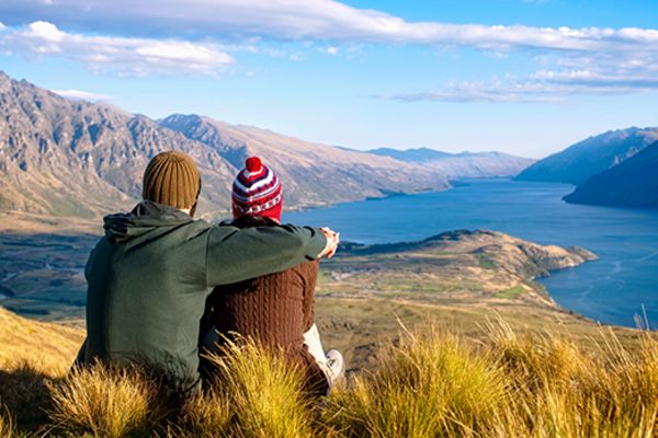 couple sitting on hill overlooking mountains and lake in queenstown