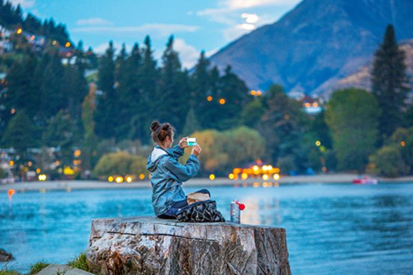 lady sitting on tree stump near lake in queenstown
