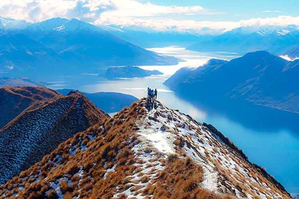 people standing on top of a mountain with lake at the base in queenstown