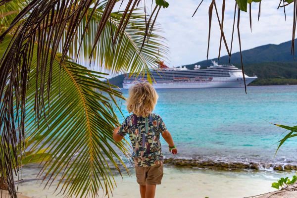 Child on beach looking out at Carnival cruise ship anchored in the distance