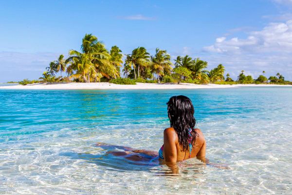 Lady sitting in shallow water looking out at the ocean/sand island in the distance