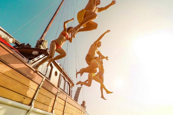 Friends jumping off a sailboat into the ocean