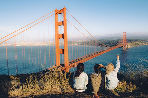 three friends sitting on edge of cliff overlooking golden gate bridge