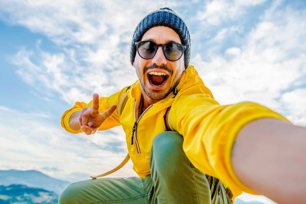 Man in a yellow jacket taking a selfie on a mountaintop
