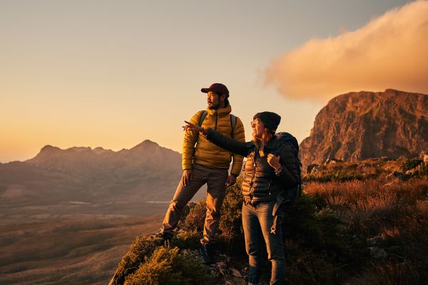 Couple in warm hiking gear standing on tall rocks looking out at the horizon