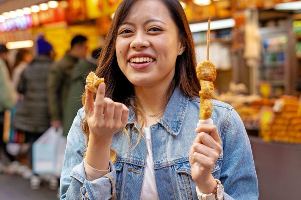 Woman eating food off a stick in a shopping street in South Korea