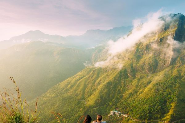 Two people sitting on a rock looking out a tall mountains and rolling mist