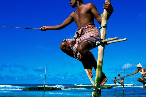 Men fishing while balancing on tall bamboo poles in the sea