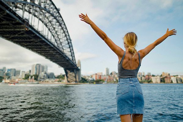 Woman raising her hands looking up at Sydney Harbour Bridge