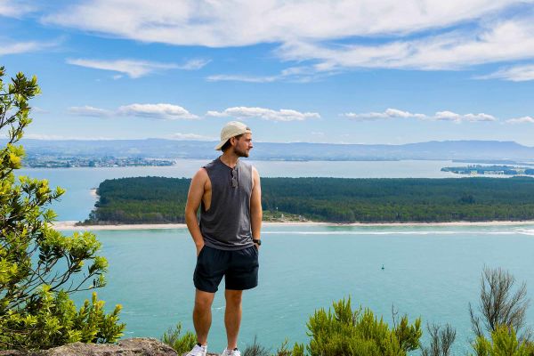 Guy standing on boulder overlooking blue water