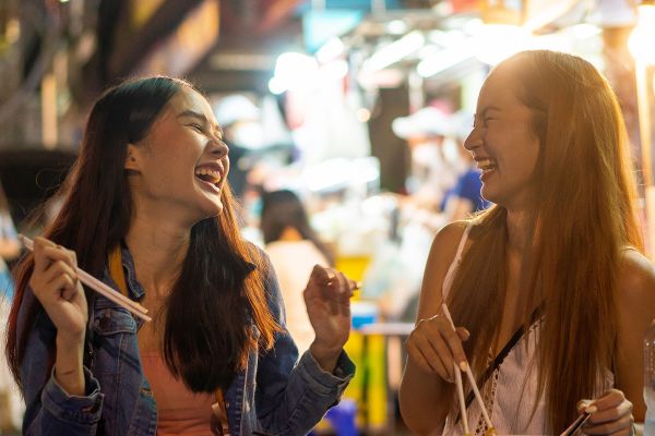 Two women laughing eating with chopsticks at night