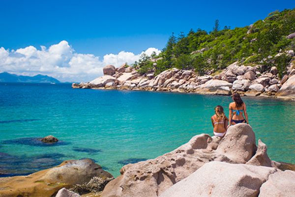 Two women in bikinis sitting on rocks, looking out at the ocean