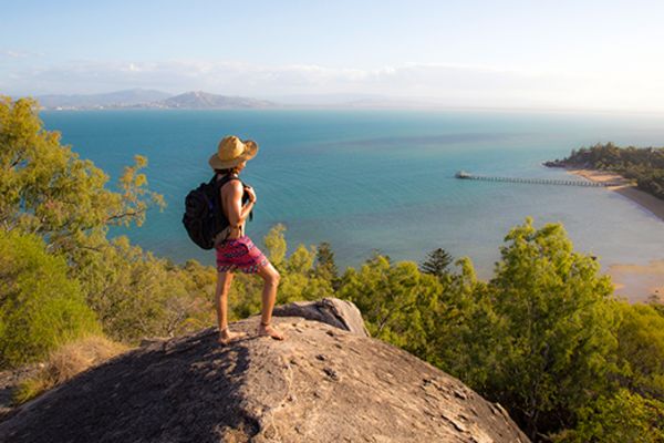 Woman with a backpack standing on a rock on a mountain, looking down at the ocean