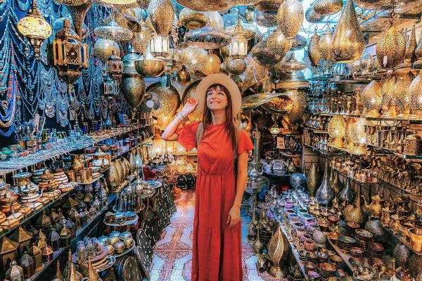 Woman in an orange dress looking at thousands of bronze lights, bowls, plates and more in a Turkish shop