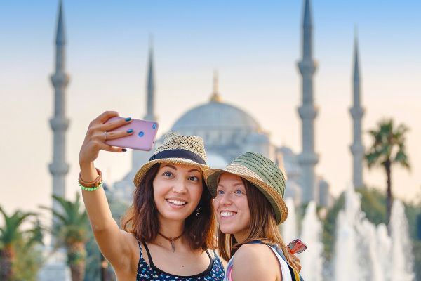 Two women posing fo a selfie in front of the Blue Mosque in Turkiye