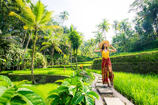 Woman walking on a thin path through a lush green field in Ubud